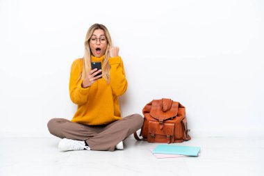 Uruguayan student woman sitting one the floor isolated on white background surprised and sending a message