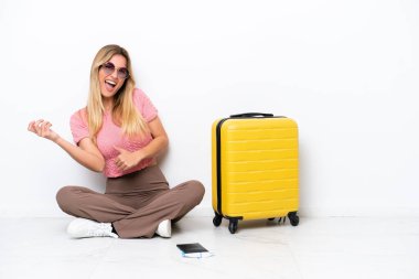 Uruguayan traveler woman sitting on the floor isolated on white background making guitar gesture