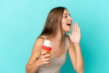 Young Lithuanian woman with cornet ice cream isolated on blue background shouting with mouth wide open to the side