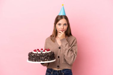 Young Lithuanian woman holding birthday cake isolated on pink background thinking