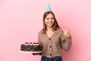Elinde doğum günü pastası tutan Litvanyalı genç bir kadın pembe arka planda izole edilmiş bir şekilde baş parmak işareti yapıyor.