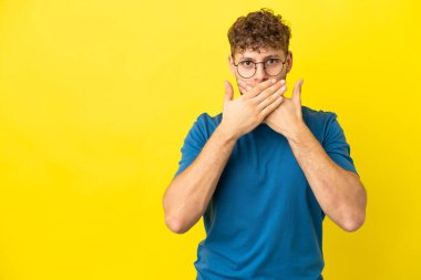 Sarı arka planda izole edilmiş yakışıklı beyaz adam elleriyle ağzını kapatıyor.