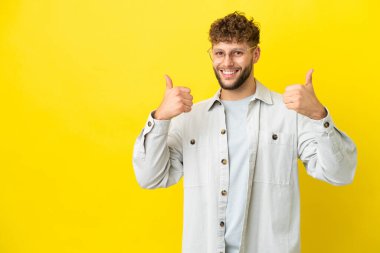 Sarı arka planda izole edilmiş yakışıklı beyaz bir adam baş parmak işareti yapıyor.