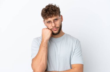 Beyaz arka planda, gözlüklü ve üzgün suratlı, beyaz tenli genç bir adam.