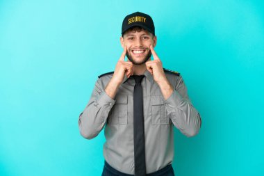 Genç güvenlik görevlisi mavi arka planda izole edilmiş mutlu ve hoş bir ifadeyle gülümsüyor.