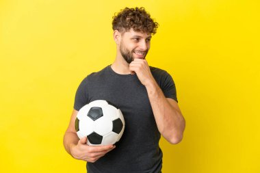 Yakışıklı genç futbolcu. Sarı arka planda izole edilmiş. Yan tarafa bakıyor ve gülümsüyor.