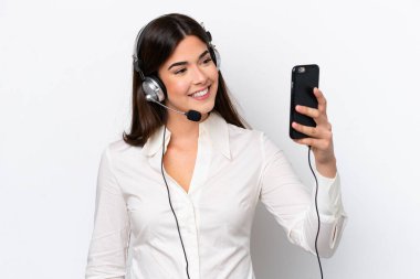 Beyaz arka planda izole edilmiş bir kulaklıkla çalışan beyaz pazarlamacı kadın selfie çekiyor.