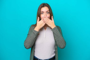 Mavi arka planda izole edilmiş genç beyaz kadın elleriyle ağzını kapatıyor.