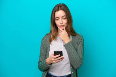 Genç beyaz kadın mavi arka planda izole edilmiş düşünüyor ve bir mesaj gönderiyor.