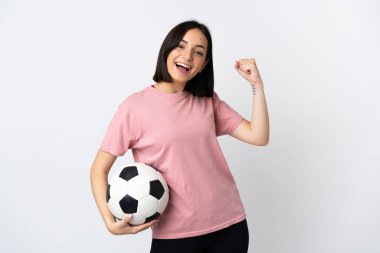 Beyaz arka planda izole edilmiş genç beyaz bir kadın futbol topuyla zaferi kutluyor.