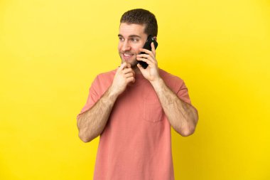 Yakışıklı sarışın adam izole edilmiş arka planda cep telefonu kullanıyor. Yan tarafa bakıyor ve gülümsüyor.