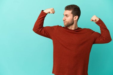 Yakışıklı sarışın, soyutlanmış mavi arka planda güçlü bir jest yapıyor.