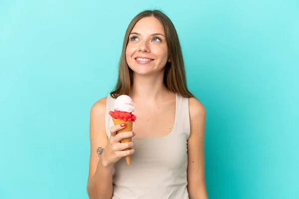 Young Lithuanian woman with cornet ice cream isolated on blue background thinking an idea while looking up