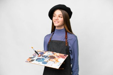 Young artist man holding a palette over isolated white background looking to the side and smiling
