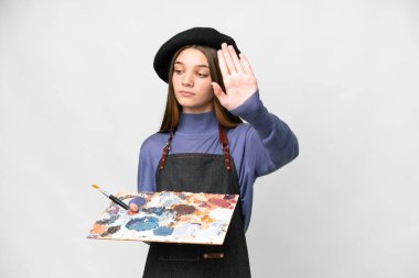 Young artist man holding a palette over isolated white background making stop gesture and disappointed