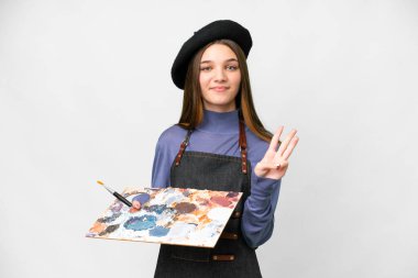 Young artist man holding a palette over isolated white background happy and counting three with fingers