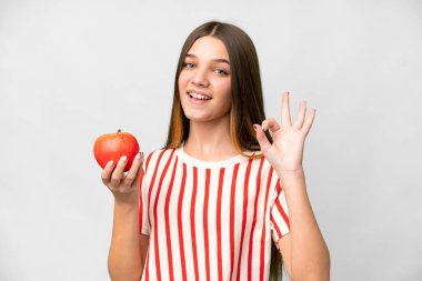 Teenager girl with an apple over isolated white background showing ok sign with fingers