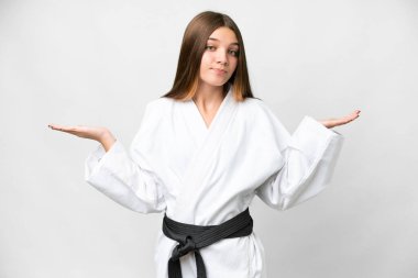 Teenager girl doing karate over isolated white background having doubts while raising hands