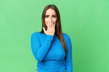 Young beautiful woman over isolated chroma key background covering mouth with hand