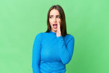 Young beautiful woman over isolated chroma key background whispering something with surprise gesture while looking to the side