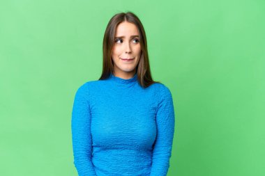 Young beautiful woman over isolated chroma key background having doubts while looking up