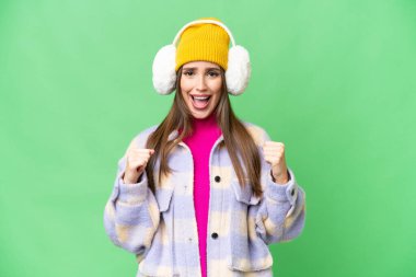 Young woman wearing winter muffs over isolated chroma key background celebrating a victory in winner position