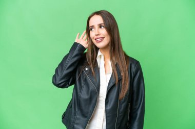 Young beautiful woman over isolated chroma key background listening to something by putting hand on the ear