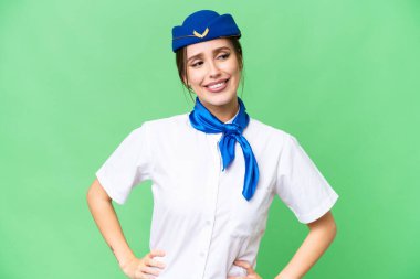 Airplane stewardess over isolated chroma key background posing with arms at hip and smiling