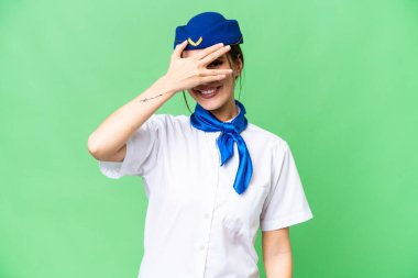 Airplane stewardess over isolated chroma key background covering eyes by hands and smiling