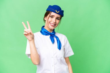 Airplane stewardess over isolated chroma key background smiling and showing victory sign