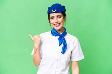 Airplane stewardess over isolated chroma key background pointing to the side to present a product