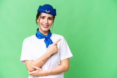Airplane stewardess over isolated chroma key background pointing to the side to present a product