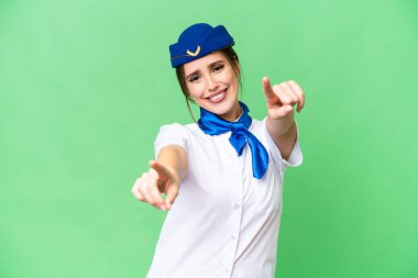 Airplane stewardess over isolated chroma key background points finger at you while smiling
