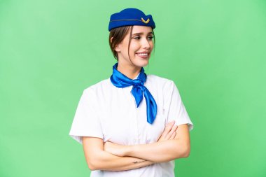 Airplane stewardess over isolated chroma key background with arms crossed and happy