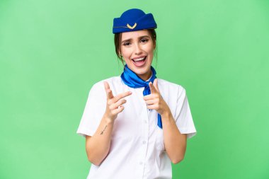 Airplane stewardess over isolated chroma key background pointing to the front and smiling