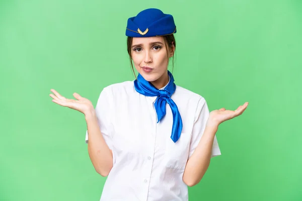 Airplane stewardess over isolated chroma key background having doubts while raising hands