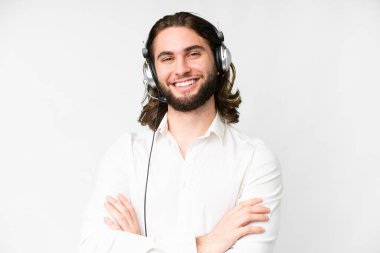 Telemarketer man working with a headset over isolated white background keeping the arms crossed in frontal position