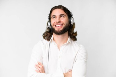 Telemarketer man working with a headset over isolated white background looking up while smiling