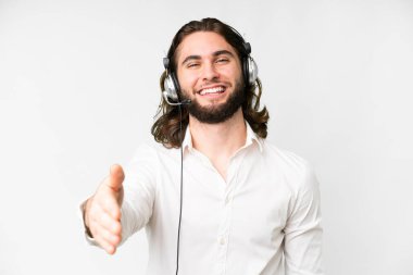 Telemarketer man working with a headset over isolated white background shaking hands for closing a good deal