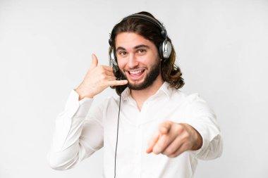 Telemarketer man working with a headset over isolated white background making phone gesture and pointing front