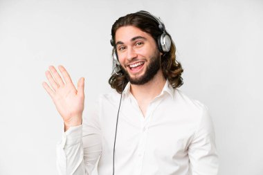 Telemarketer man working with a headset over isolated white background saluting with hand with happy expression