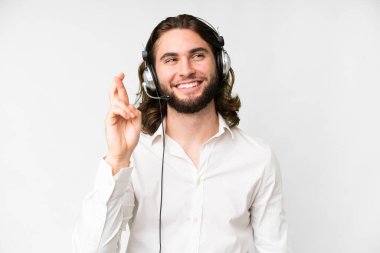 Telemarketer man working with a headset over isolated white background with fingers crossing and wishing the best