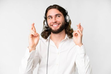 Telemarketer man working with a headset over isolated white background with fingers crossing