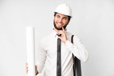 Young architect man with helmet and holding blueprints over isolated white background thinking an idea while looking up
