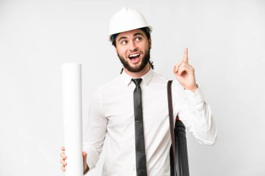 Young architect man with helmet and holding blueprints over isolated white background thinking an idea pointing the finger up