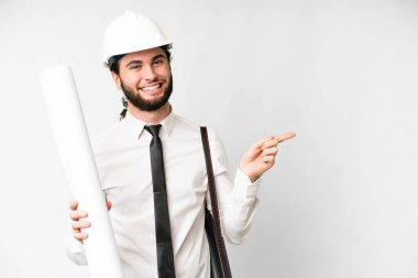 Young architect man with helmet and holding blueprints over isolated white background pointing finger to the side
