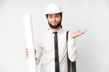 Young architect man with helmet and holding blueprints over isolated white background having doubts while raising hands