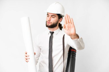 Young architect man with helmet and holding blueprints over isolated white background making stop gesture and disappointed