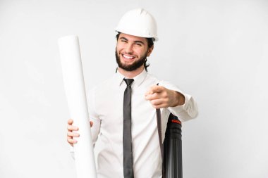 Young architect man with helmet and holding blueprints over isolated white background pointing front with happy expression