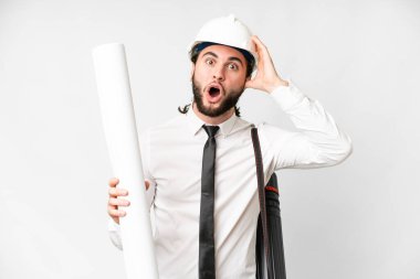 Young architect man with helmet and holding blueprints over isolated white background with surprise expression